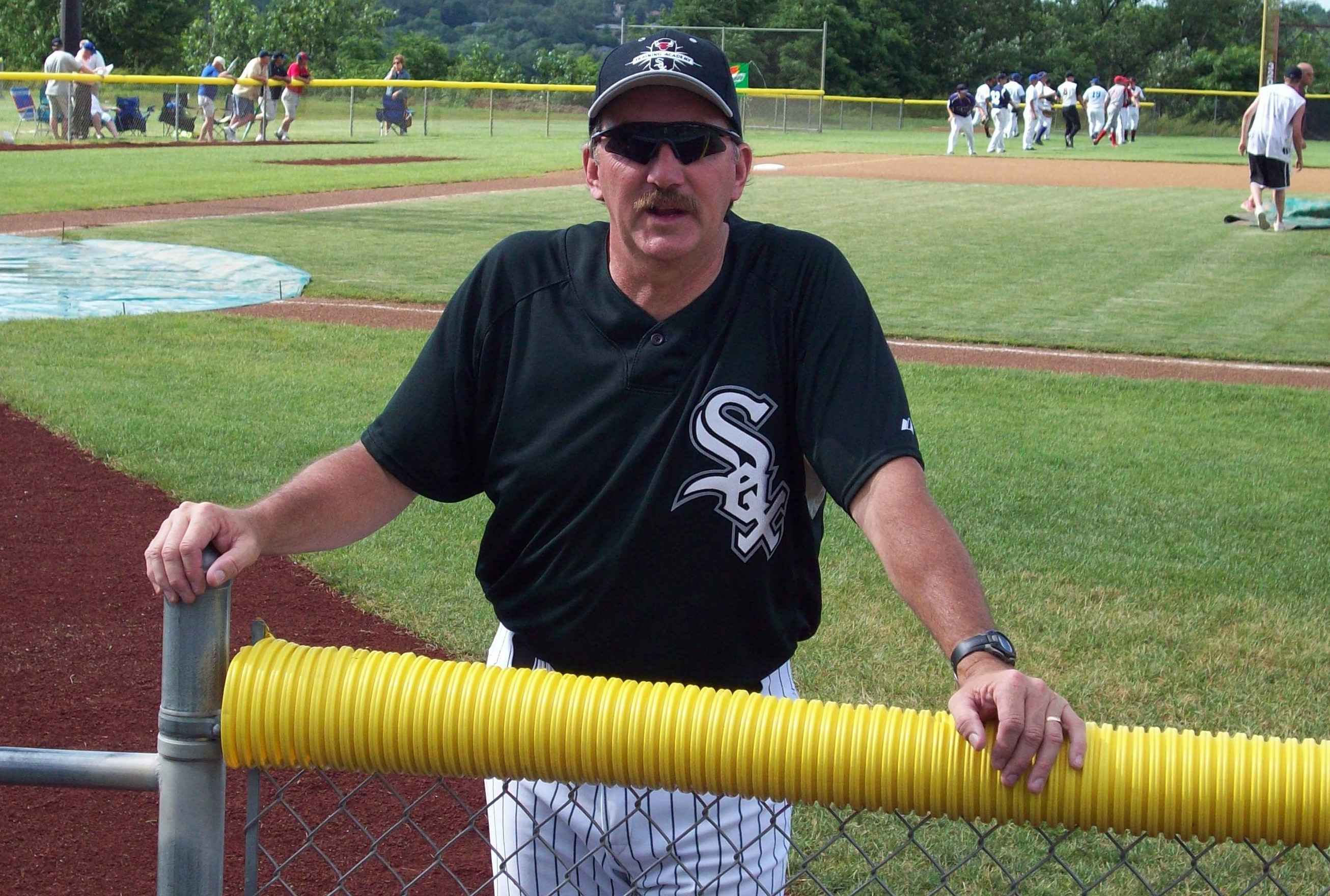 Phil Fox in a Sox uniform leaned up against chain link fence at the baseball field