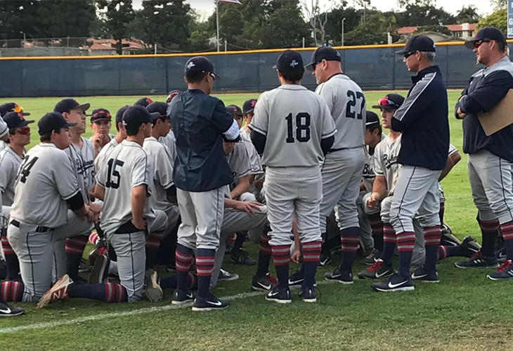 Baseball coach talking to his team as they are huddled in a circle on the first base line