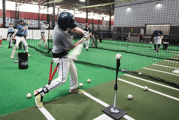 Multiple youth baseball players swinging bats inside indoor facility