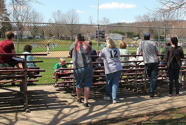 Parents leaning on bleachers watching youth baseball game
