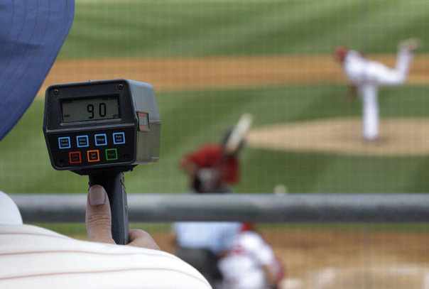 Radar gun reading 90 in the foreground with blurred pitcher throwing to batter in background