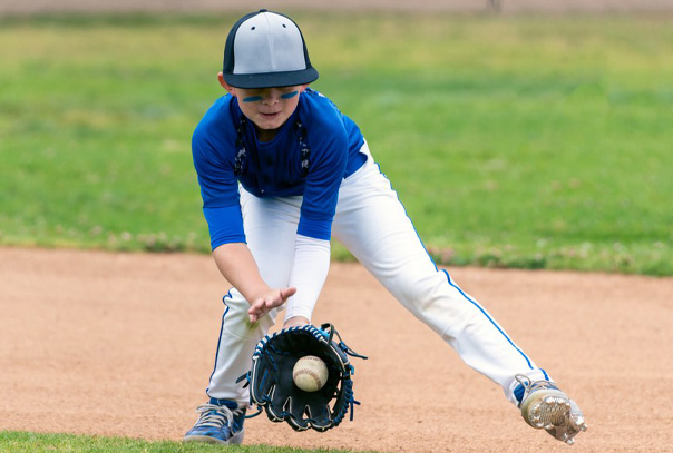 Youth baseball infielder in blue jersey fielding a ground ball