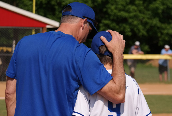 A coach with his arm around a youth player having a conversation on the mound