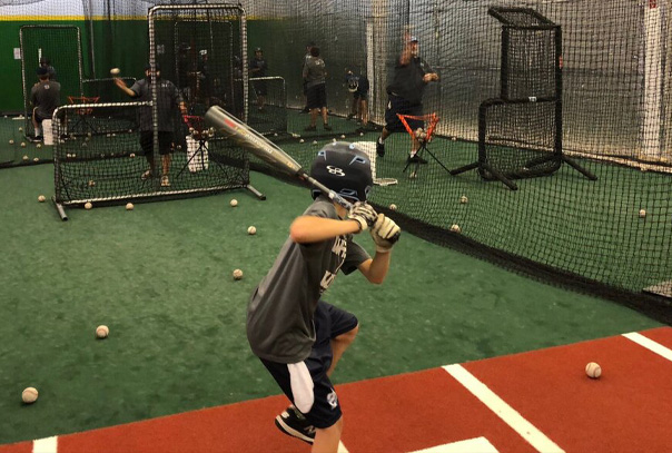 A youth player taking batting practice at an indoor facility