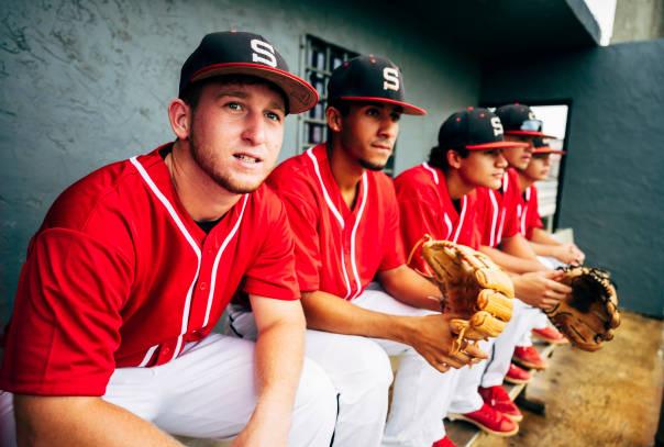 Three players in red jerseys sitting on a bench in dugout