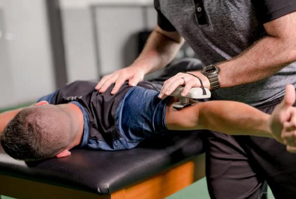A man lying face down on training table with athletic trainer working on arm