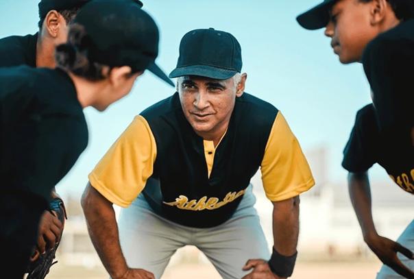 Coach bent down with hands on knees talking to four of his youth aged players