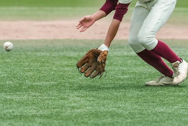 A baseball on grass traveling towards a glove on a player's hands. Only see the arm with glove and legs of the player.
