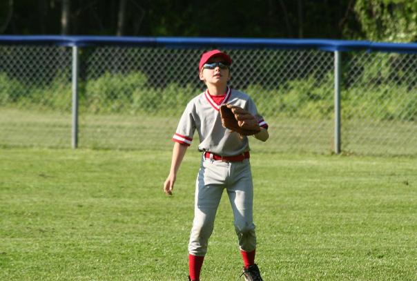 Youth outfielder with glove up in outfield in front of chain link outfield fence