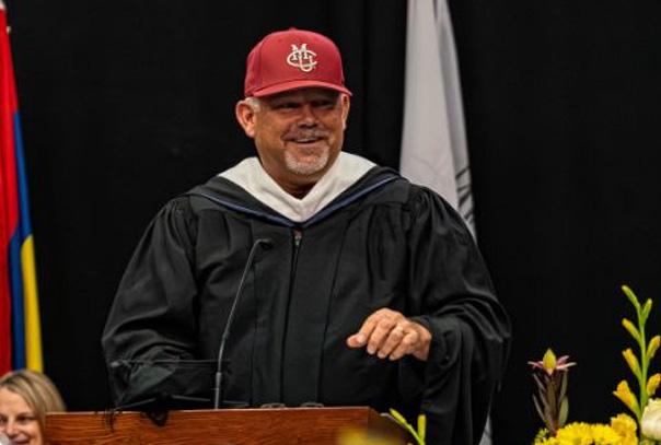 Chris Hanks in graduation gown and CMU baseball hat speaking at podium during graduation